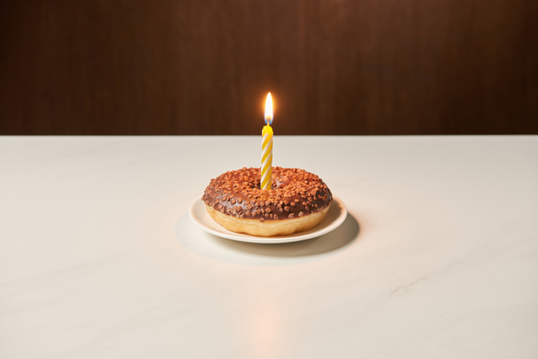 burning candle in middle of sweet doughnut with icing and sprinkles on white table  - Foto, immagini