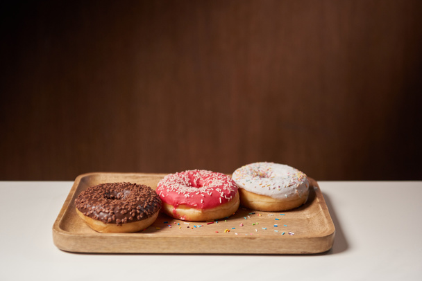 tasty donuts with icing and sprinkles on wooden cutting board - Foto, Imagem