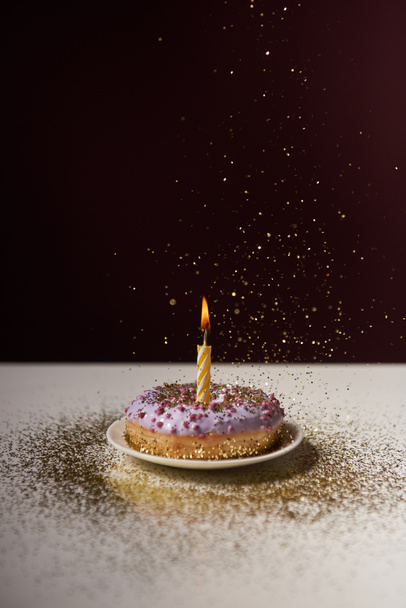 burning candle in middle of sweet doughnut with falling sparkles isolated on black - Photo, image