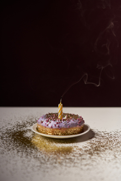 свічка в середині смачного пончика з блискучими блискітками на білому столі ізольовані на чорному
 - Фото, зображення