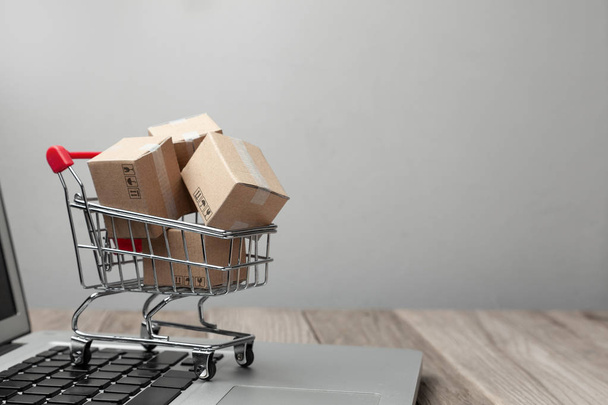 Delivery of the order from the online store. Online shopping. Boxes with goods in the shopping basket on the table with laptop. Copy space for text. - Фото, зображення