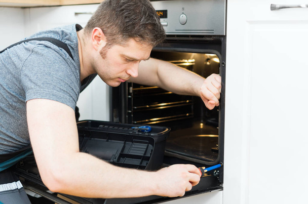 Professionele klusjesman in overalls herstellen van binnenlandse oven in de keuken. - Foto, afbeelding