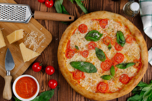 top view of pizza with tomatoes, cheese and fresh basil leaves served on wooden table - Fotoğraf, Görsel