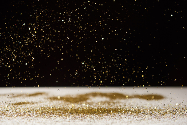 selective focus of bright sparkles falling on white table isolated on black  - Fotoğraf, Görsel