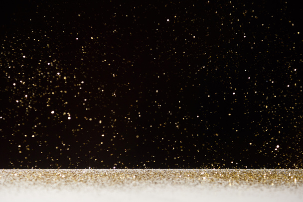selective focus of golden sparkles falling on white table isolated on black  - Photo, Image