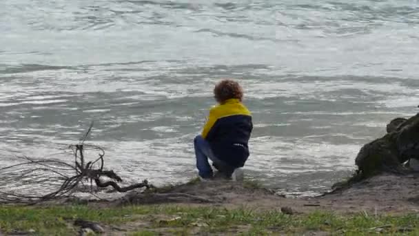 young boy with curly hairs playing near the river at autumn - Imágenes, Vídeo