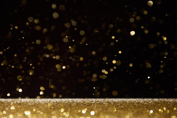 selective focus of golden shiny sparkles falling on table isolated on black  - Foto, Bild
