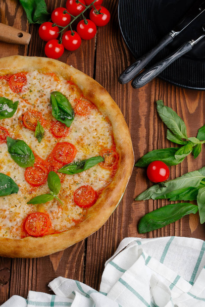 bovenaanzicht van pizza met tomaten, kaas en verse basilicum laat geserveerd op houten tafel - Foto, afbeelding