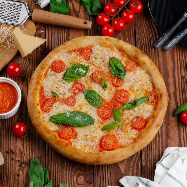 üstten görünüm Pizza domates, peynir ve taze fesleğen ile ahşap masaya servis bırakır - Fotoğraf, Görsel