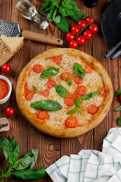 pohled shora Pizza s rajčaty, sýrem a čerstvou bazalkou listy servírované na dřevěný stůl - Fotografie, Obrázek