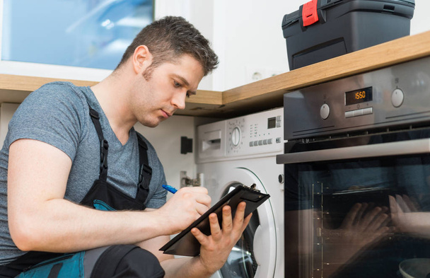 Handyman doing inspection of washing machine in the kitchen. - Valokuva, kuva