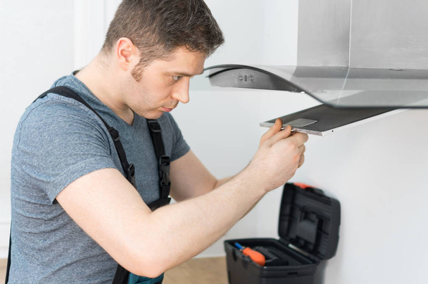 Handsome foreman fixing exhaust hood in the kitchen. - Photo, Image