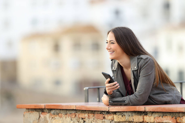 Mulher feliz segurando telefone inteligente contemplando paisagem ao ar livre em uma cidade periferia
 - Foto, Imagem