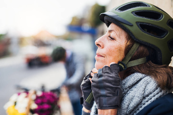 Active senior woman standing outdoors in town, putting on a bike helmet. Copy space. - Fotó, kép