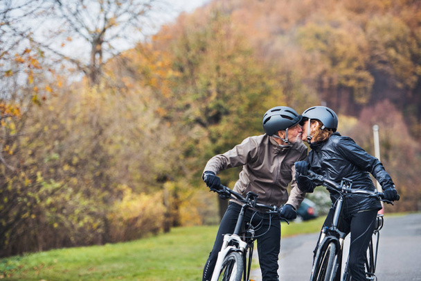 Active senior couple with electrobikes standing outdoors on a road in nature, kissing. - Foto, immagini