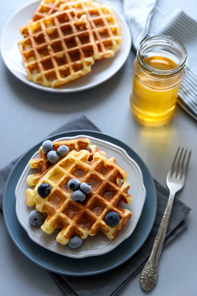 Belgian waffles with blueberries and honey on gray wooden background. Homemade healthy breakfast. Selective focus - Photo, Image