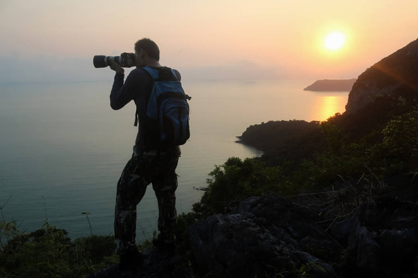 Silhouette of man climbing rock, Photographer on the mountain at sunrise ,Archipelago island in Thailand - Photo, Image