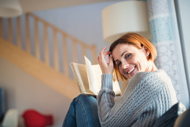 Una giovane donna seduta in casa su un divano, a leggere un libro
. - Foto, immagini