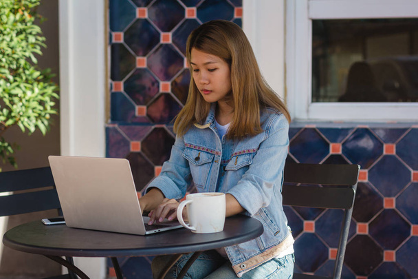 Asian young women in smart casual clothes working sending email on laptop and drinking coffee while sitting in cafe. Lifestyle women communication and working in coffee shop concept. - Photo, Image