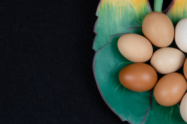 Vista superior de ovos de galinha em uma placa em forma de folha e em um fundo preto
. - Foto, Imagem