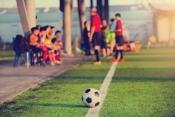 μπάλα ποδοσφαίρου στο touchlines σχετικά με τεχνητό χλοοτάπητα με θολή ποδόσφαιρο παίκτες και προπονητής προπόνηση στο παιχνίδι. - Φωτογραφία, εικόνα