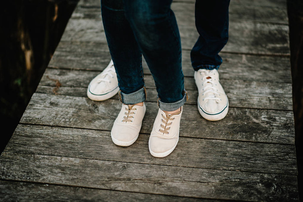 legs in sneakers of husband and wife on wooden bridge near lake - Photo, Image