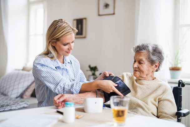 A health visitor measuring a blood pressure of a senior woman at home. - Valokuva, kuva