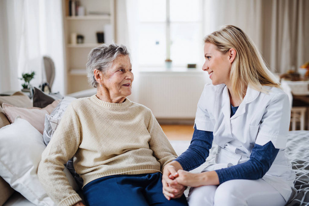 A health visitor talking to a sick senior woman sitting on bed at home. - Foto, Bild