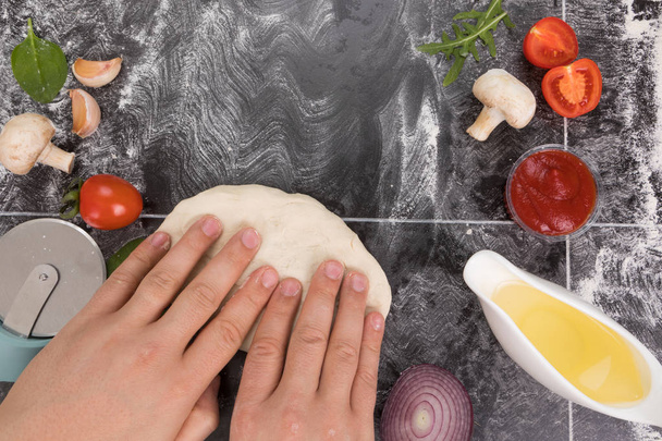 Ingredients for pizza, mushrooms, tomatoes, onion, rucola, basil, garlic, oil dough tomato sauce and flour Hands preparing the dough - Φωτογραφία, εικόνα