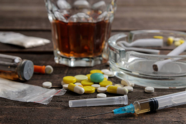 Kahverengi ahşap bir masada alkol, sigara ve uyuşturucu gibi çeşitli bağımlılık yapıcı uyuşturucular. Uyuşturucu bağımlılığı kavramı - Fotoğraf, Görsel