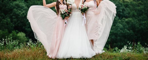 νύφη και παράνυμφων στην κομψά φορέματα στέκεται και κρατώντας μπουκέτα με παστέλ ροζ λουλούδια - Φωτογραφία, εικόνα