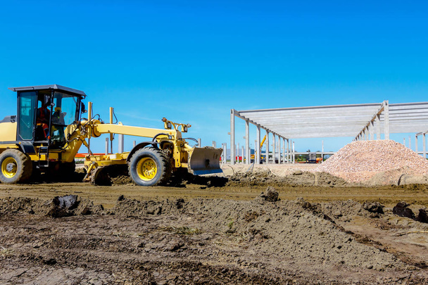 El operador está conduciendo una niveladora amarilla, nivelando el terreno en el sitio de construcción. - Foto, Imagen