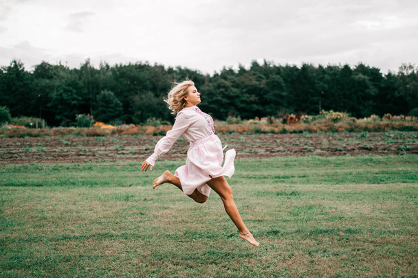 slender girl jumping on grass against pine trees background - Foto, afbeelding