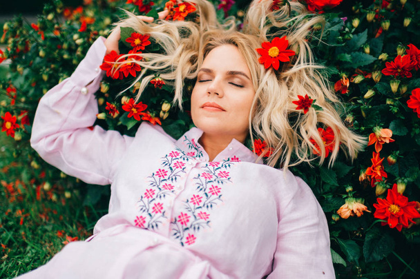 beautiful blond woman in embroidered dress lying in flowers - Foto, Bild