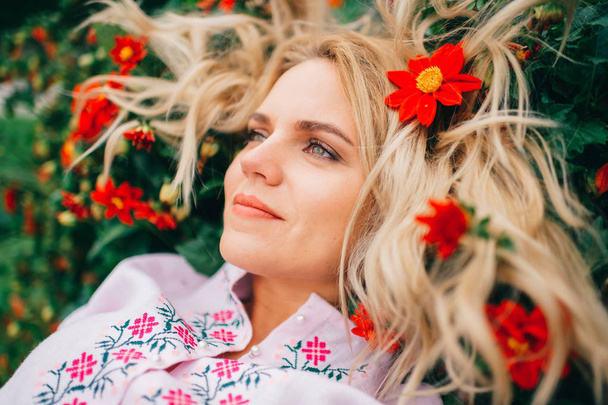 beautiful blond woman in embroidered dress lying in flowers - Fotoğraf, Görsel