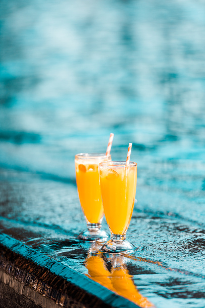 orange cocktails with straws standing near swimming pool - Foto, imagen