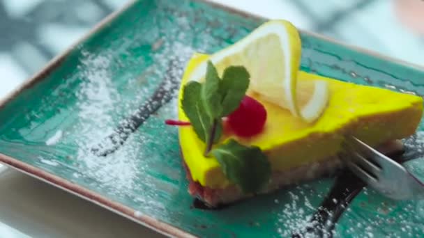 Cup of pink latte coffee with yellow lemon dessert with cherry, mint and fork on green plate in a cafe - Záběry, video