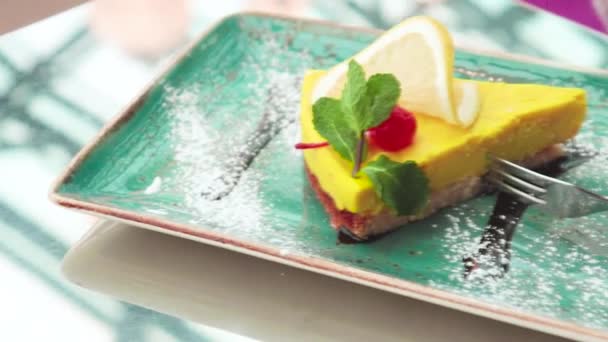 Cup of pink latte coffee with yellow lemon dessert with cherry, mint and fork on green plate in a cafe - Filmati, video