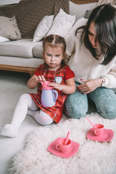 Happy loving family. Mother and her daughter girl play tea-party and drink tea from cups in children room. Funny mom and lovely child having fun indoors - Foto, Bild