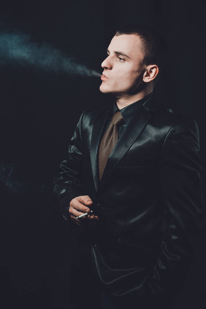 egy fiatal férfi dohányzik egy cigarettát, egy fekete háttér, a klasszikus fekete öltönyt 2019 - Fotó, kép
