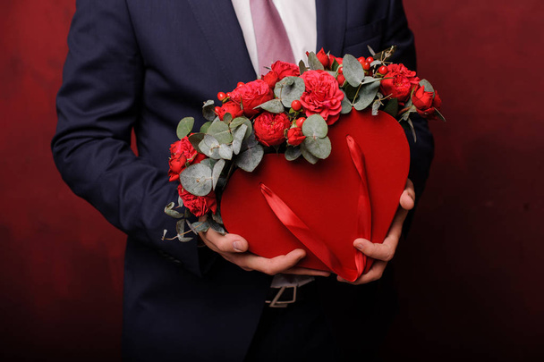 Homem de terno segurando em uma mão uma caixa vermelha de belas rosas
 - Foto, Imagem