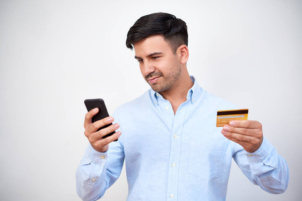 Молодой человек с темными волосами, держащий смартфон и кредитную карту и платить онлайн изолированы на белом фоне
 - Фото, изображение