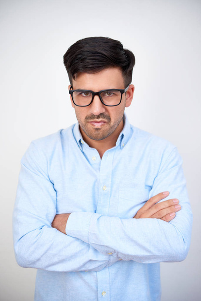 Портрет разгневанного молодого человека в очках, нахмуренного и смотрящего на камеру на белом фоне
 - Фото, изображение