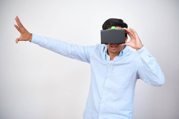 Retrato de jovem de camisa vestindo realidade virtual headset 3D e explorando a peça em pé sobre fundo branco
 - Foto, Imagem