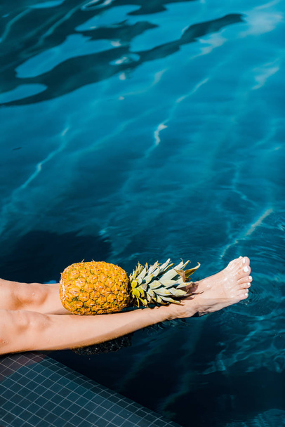 low section view of girl posing with sweet pineapple at poolside - Foto, Bild
