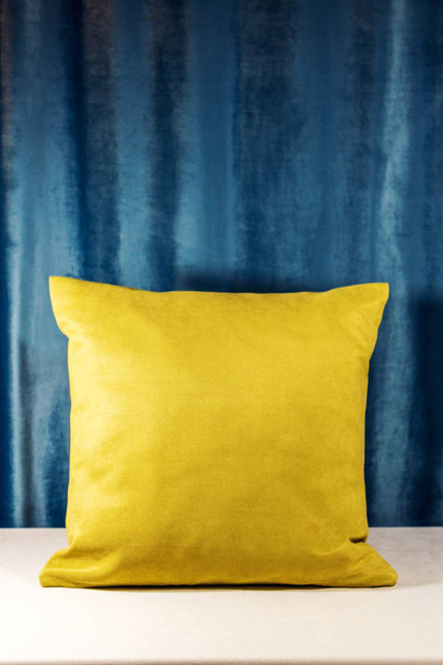 Yellow pillow stanfing on a table covered in a white velvet material. Blue background. Soft and warm lightsource - Photo, Image