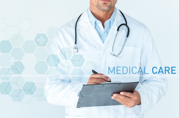 bijgesneden afbeelding van arts met de stethoscoop op schouders schrijven iets in klembord geïsoleerd op wit met medische zorg interface - Foto, afbeelding