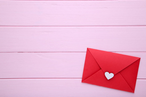 Red envelope with white heart on pink wooden background - Fotoğraf, Görsel