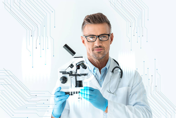 guapo científico en gafas sosteniendo microscopio y mirando a la cámara en blanco con interfaz de tecnología
 - Foto, Imagen