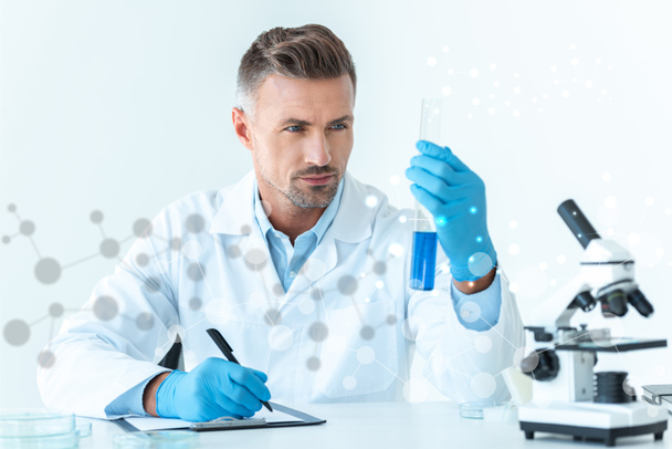 guapo científico mirando el tubo de ensayo con reactivo azul
  - Foto, Imagen